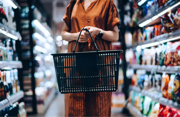 Cropped shot of young woman carrying a shopping basket, standing along the product aisle, grocery shopping for daily necessities in supermarket