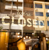 Closed sign hanging in business window by a string - crooked with glob of glue also attaching it to window