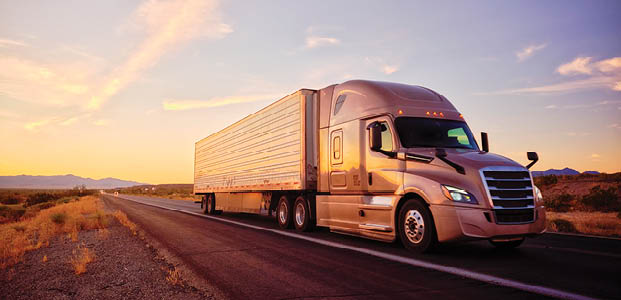 Large semi truck hauling freight on the open highway in the western USA under an evening sky.